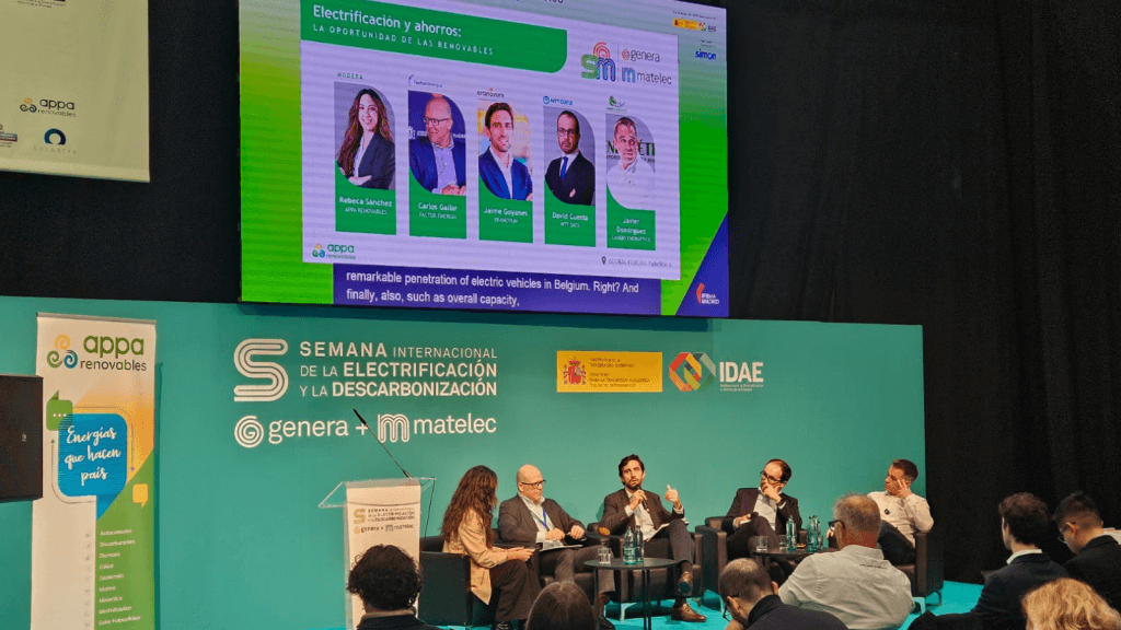 Panell d'experts durant la taula rodona de APPA Renovables en GENERA 2025, sobre electrificació i estalvis, amb ponents debatent enfront de l'audiència i una pantalla amb informació de l'esdeveniment.