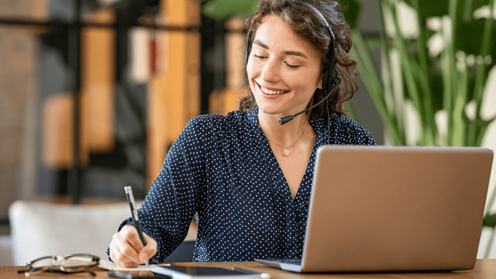 Agente de atención al cliente sonriente con auriculares y micrófono trabajando frente a su portátil, representando un servicio técnico y humano en el sector energético