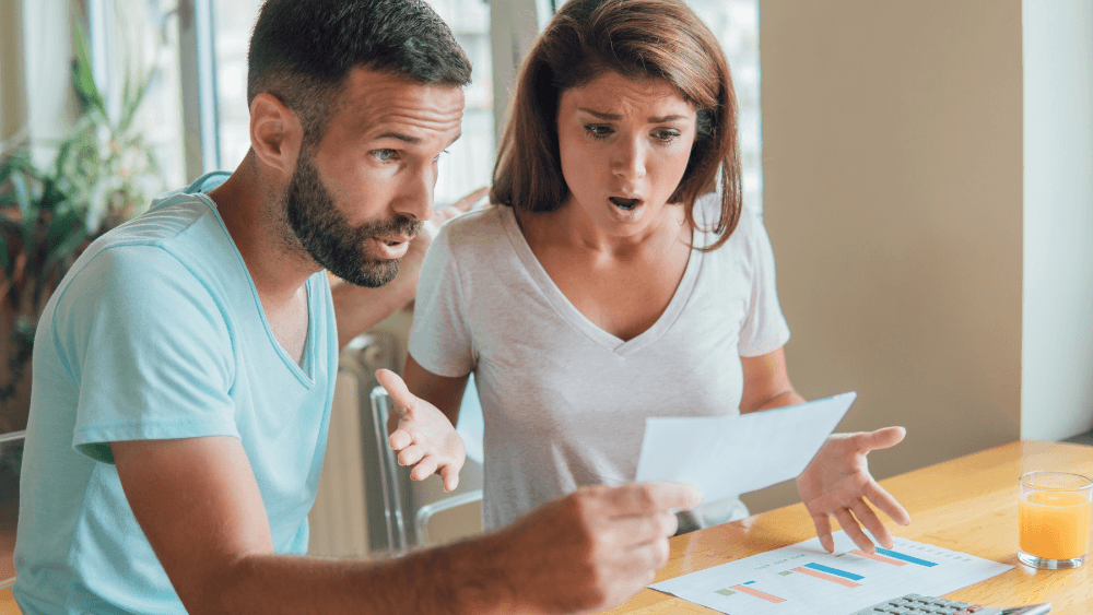 Pareja con expresión de sorpresa y preocupación revisando una factura de luz elevada, ilustrando el miedo común a los mitos sobre el precio y el riesgo de la tarifa variable de luz