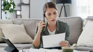 Mujer preocupada revisando una factura de la luz mientras habla por teléfono para evitar errores al elegir la potencia contratada.